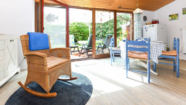 A room with a rocking chair, a dining table with chairs, a refrigerator, and a view of the outdoors. - Holiday house North Sea snail (Esens)
