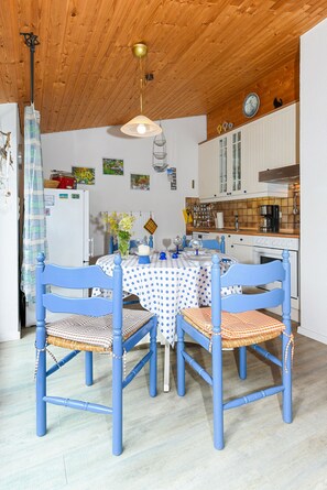 A dining area with a wooden ceiling, a white refrigerator, and a kitchen with white cabinets and a tiled backsplash.