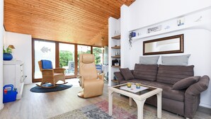 A modern living room with a wooden ceiling, a brown sofa, a rocking chair, and a coffee table. - Holiday house North Sea snail (Esens)