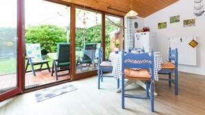 A dining area with a wooden ceiling, large windows, and a view of greenery outside. - Holiday house North Sea snail (Esens)
