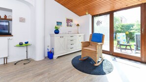 A modern interior with a wooden ceiling, white walls, a dining area with a table and chairs, and a large sliding glass door leading to an outdoor patio. - Holiday house North Sea snail (Esens)