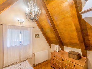 Cozy attic bedroom with a sloped ceiling, chandelier, dresser, and radiator.