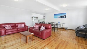 Un vaste espace de vie comprenant un ensemble de canapés en cuir rouge, une table basse en bois et un coin repas avec une table et des chaises blanches.
