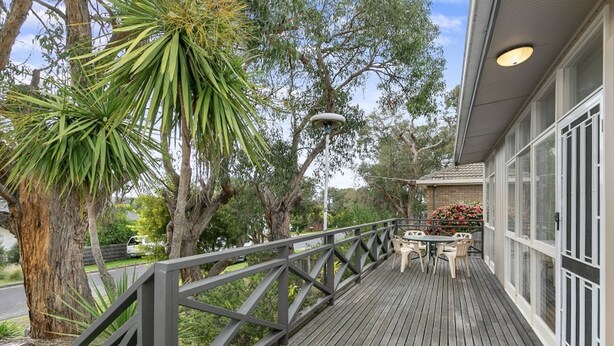 Une terrasse en bois avec une rambarde, une table entourée de chaises et un bâtiment doté de grandes fenêtres.
