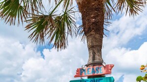 A wooden signpost with colorful signs attached, located beside a wooden walkway with a view of the ocean. - Beautiful condo for families, couples, and friends. (Madeira Beach)