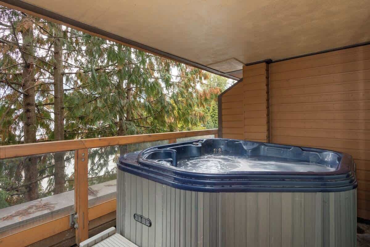 A hot tub on a balcony with wooden railings and a view of trees.