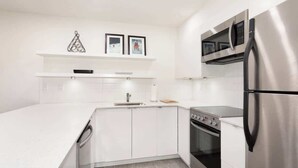 A modern kitchen with white cabinetry, a stainless steel refrigerator, a microwave, and an oven. - Cozy condo w/ hot tub & fireplace near lifts (Whistler)