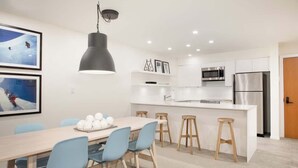 A modern kitchen with white cabinets, stainless steel appliances, and a central island with stools. - Cozy condo w/ hot tub & fireplace near lifts (Whistler)