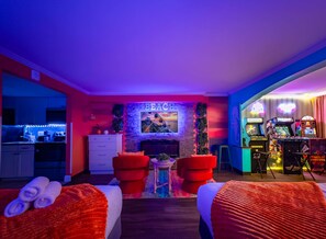 A modern hotel room with a kitchen, a fireplace, and gaming consoles.
