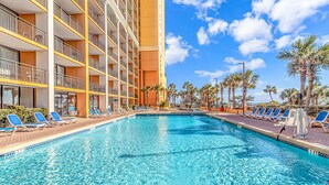 A hotel pool with multiple levels of balconies, sun loungers, and palm trees.