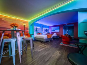 Quarto de hotel moderno com teto curvo, uma cama grande, uma escrivaninha com cadeira e uma televisão.