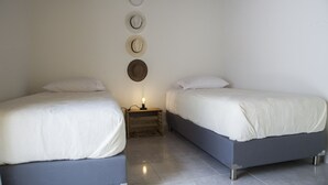 Een slaapkamer met twee bedden, een nachtkastje met een lamp, en vier hoeden aan de muur.
