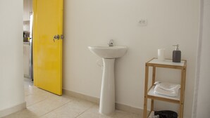 Een badkamer met een gele deur, een wit wastafelmeubel en een houten plank met handdoeken.