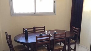 Ein Essbereich mit einem runden Tisch und sechs Stühlen, ein Fenster darüber und eine Tür zur rechten Seite.