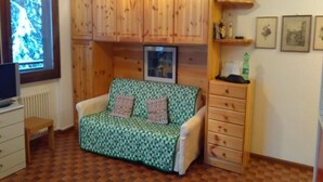 Ein gemütliches Zimmer mit einem grün gemusterten Sofa, Holzschränken, einem kleinen Holztisch und einer Heizung.