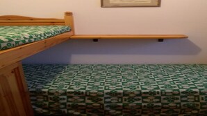 Ein Zimmer mit einem Etagenbett, einem kleinen Regal und einem gemusterten Boden.