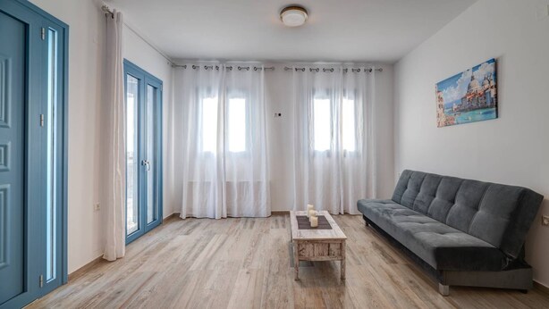 Una sala de estar con un sofá gris, una mesa de centro de madera y cortinas blancas.