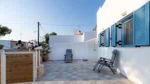 Un patio con piso a cuadros, una verja de madera, una silla de descanso y un muro con contraventanas azules.