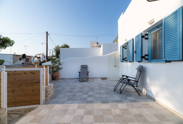 A patio with a checkered floor, a wooden gate, a lounge chair, and a wall with blue shutters. - Quiet place for special vacations for couples! (Heraklion)