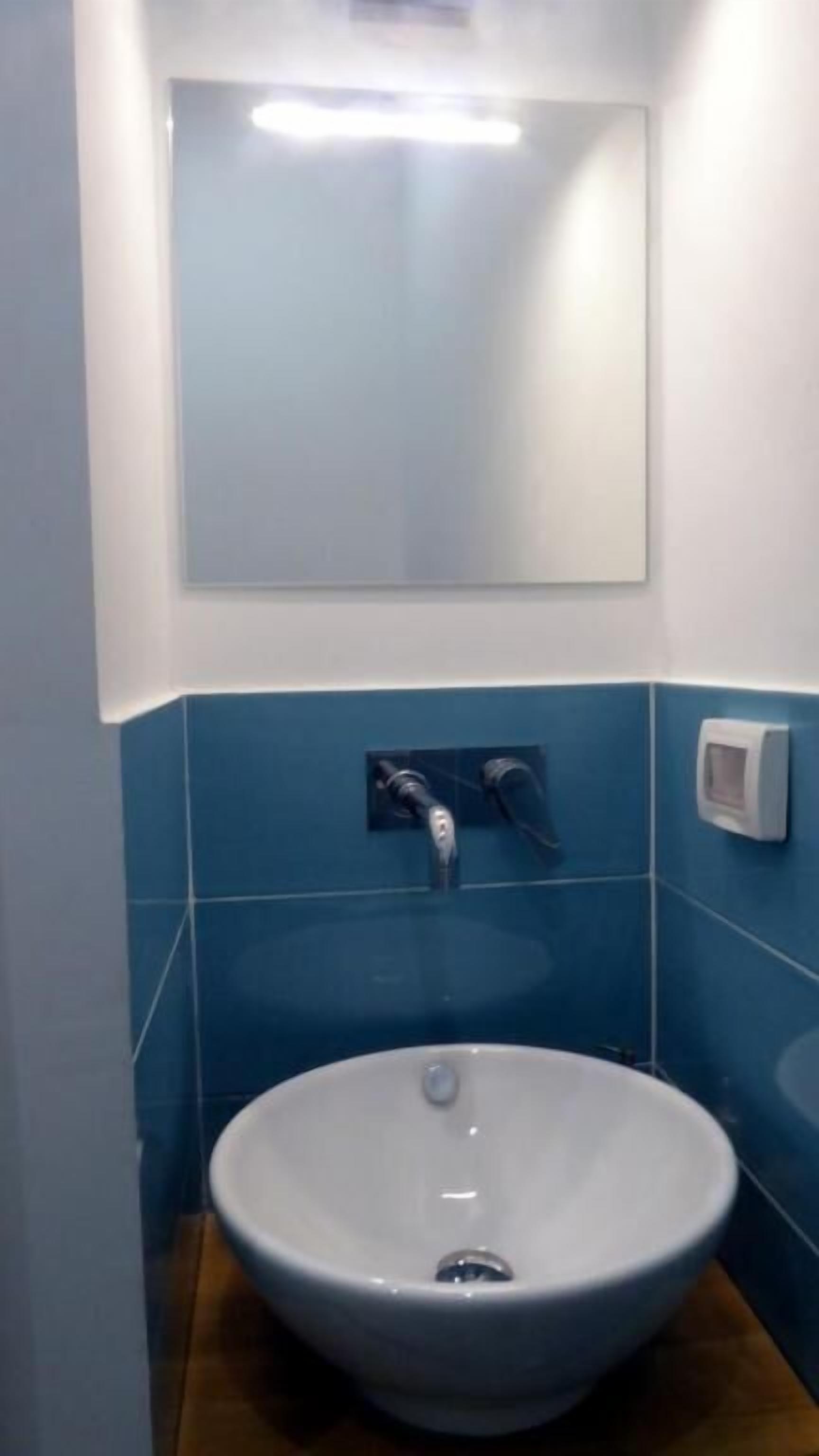 A bathroom with a white sink, blue tiles, and a mirror above it.