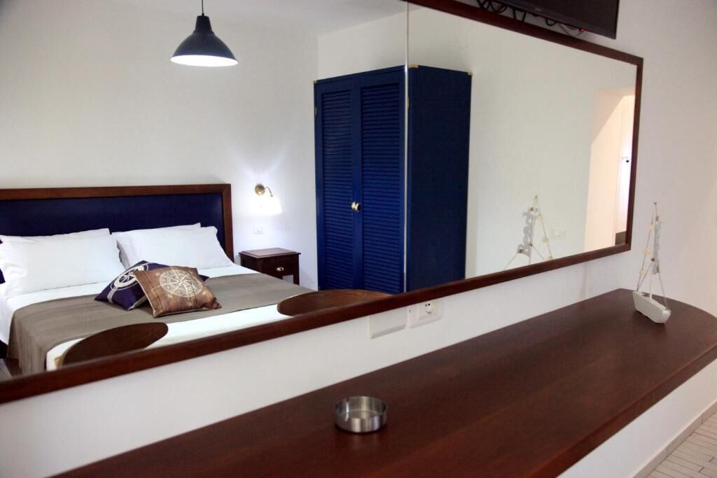 Ein Hotelzimmer mit einem großen Bett, einem hölzernen Kopfteil, einem Nachttisch, einem blauen Kleiderschrank, einem großen Spiegel und einem Holzkonsolentisch.