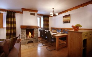A cozy dining area with a stone fireplace, wooden furniture, and a chandelier.