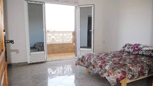 A bedroom with a bed, a door leading to an outdoor balcony, and a tiled floor. - Apartment 3 combining countryside and sea (Hadjadj)