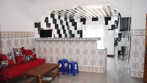 A living room with a red sofa, blue stools, a wooden coffee table, patterned wallpaper, and a kitchen area with a black and white backsplash. - Apartment 3 combining countryside and sea (Hadjadj)