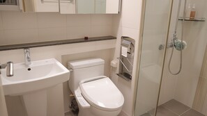 Bathroom features a sink, toilet, and glass-enclosed shower area with a handheld showerhead.