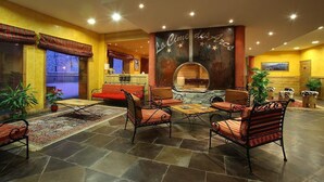Un'ampia hall con un divano rosso, diverse poltrone, un tavolino da caffè e una parete decorativa con uno specchio circolare.