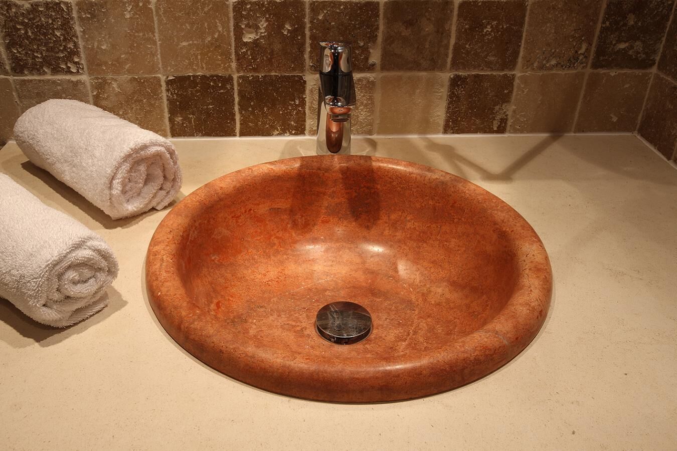 A bathroom with a round copper sink, a faucet, and two rolled towels.