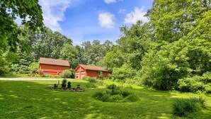 Uma casa vermelha com um gramado e jardim bem cuidados, cercada por árvores verdes densas.
