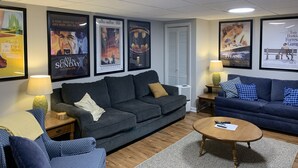 Uma sala de estar com dois sofás, uma mesa de centro e pôsteres de filmes emoldurados na parede.