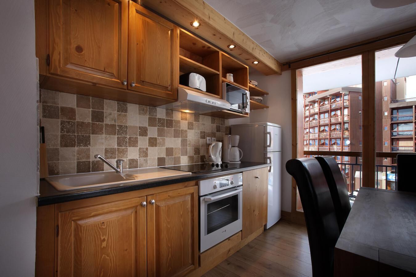 Una cocina con gabinetes de madera, salpicadero de azulejos, un lavamanos, una estufa y un refrigerador.