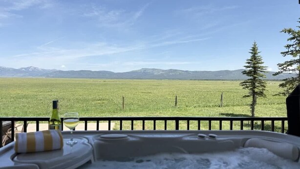 Een bubbelbad op een balkon met uitzicht op een groen veld en bergen.