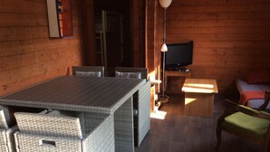 Interno di una baita in legno con un tavolo da pranzo, sedie in vimini, un televisore e un piccolo tavolino.