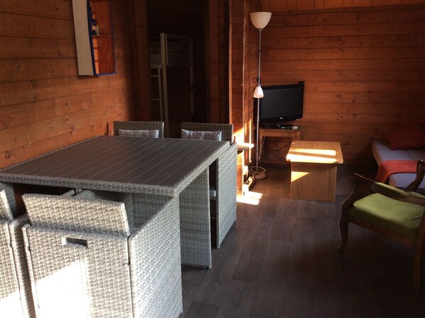 L’intérieur d’un chalet en bois comprend une table à manger, des chaises en osier, un téléviseur et une petite table en bois.