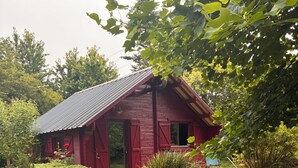 Una casa in legno rossa con tetto in metallo, circondata da un prato curato e diversi arbusti.