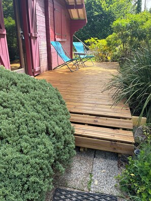Una terraza de madera con un pequeño espacio de estar, rodeada de vegetación.