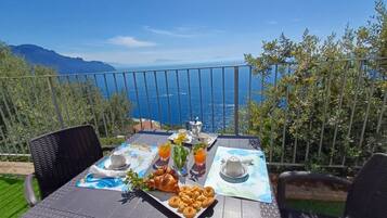 Ein Esstisch mit Frühstücksgebäck, Croissants, Teilchen und Orangensaft auf einem Balkon mit Meerblick.