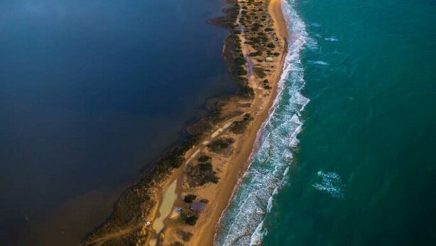Vista aérea de una zona costera con una extensa playa, una clara separación de tierra y agua, y una línea de costa distante.