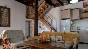 Una sala de estar acogedora con una mesa de madera, dos sofás estampados, una escalera y una zona de cocina.
