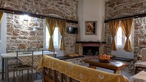 Una habitación rústica con paredes de piedra, chimenea, una mesa de comedor con sillas y un sofá.