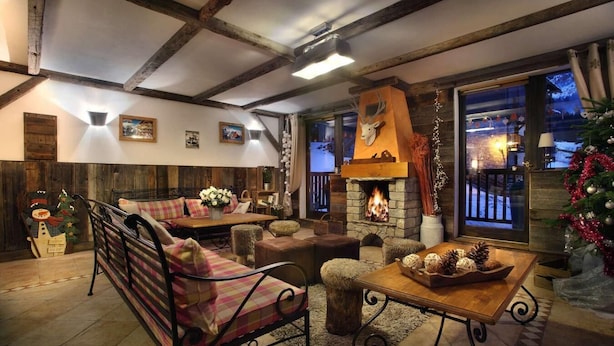 Ein gemütliches Wohnzimmer mit Kamin, Holzbalken und einem großen Fenster mit Blick auf eine verschneite Landschaft.