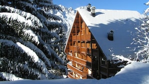 Eine Holzhütte mit einem steilen Dach, umgeben von schneebedeckten Bäumen und Bergen.