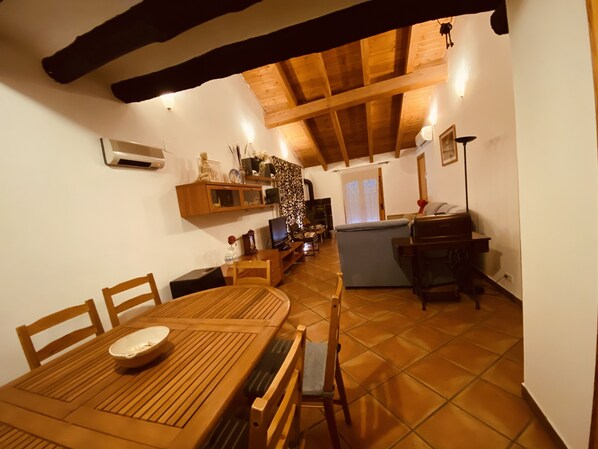 Uma sala de estar aconchegante com teto de madeira, uma mesa de jantar com cadeiras, um sofá e uma televisão.