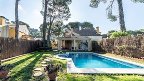 Un jardin avec une piscine, un patio couvert et une pelouse bien entretenue agrémentée de pas japonais.