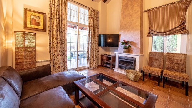 Un salon avec un canapé en cuir, une table basse en verre, des fauteuils en osier, une cheminée et un téléviseur.