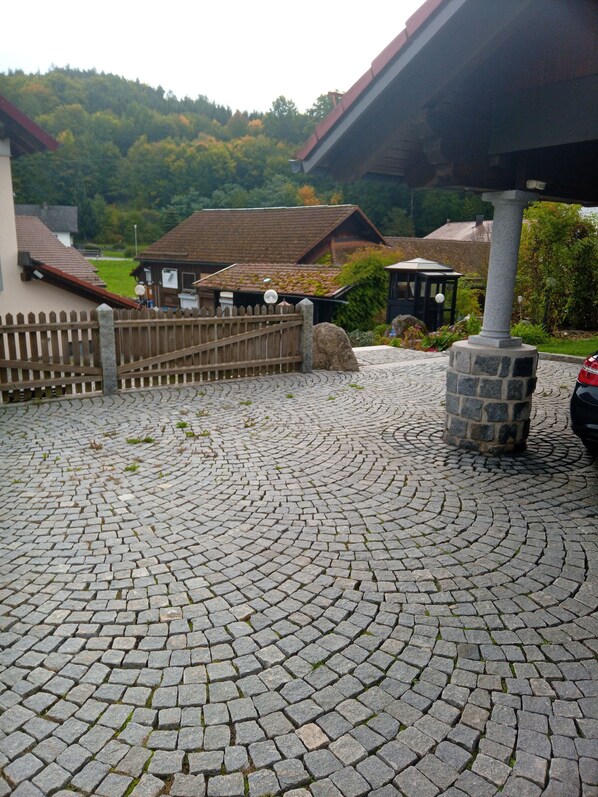 A cobblestone driveway leading to a building with a wooden fence and a stone pillar.