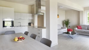 A modern kitchen with a built-in oven, a dining area with a table and chairs, and a living room with a sofa and a coffee table. - Villa with park, private pool and lovely lake view (Gardone Riviera)